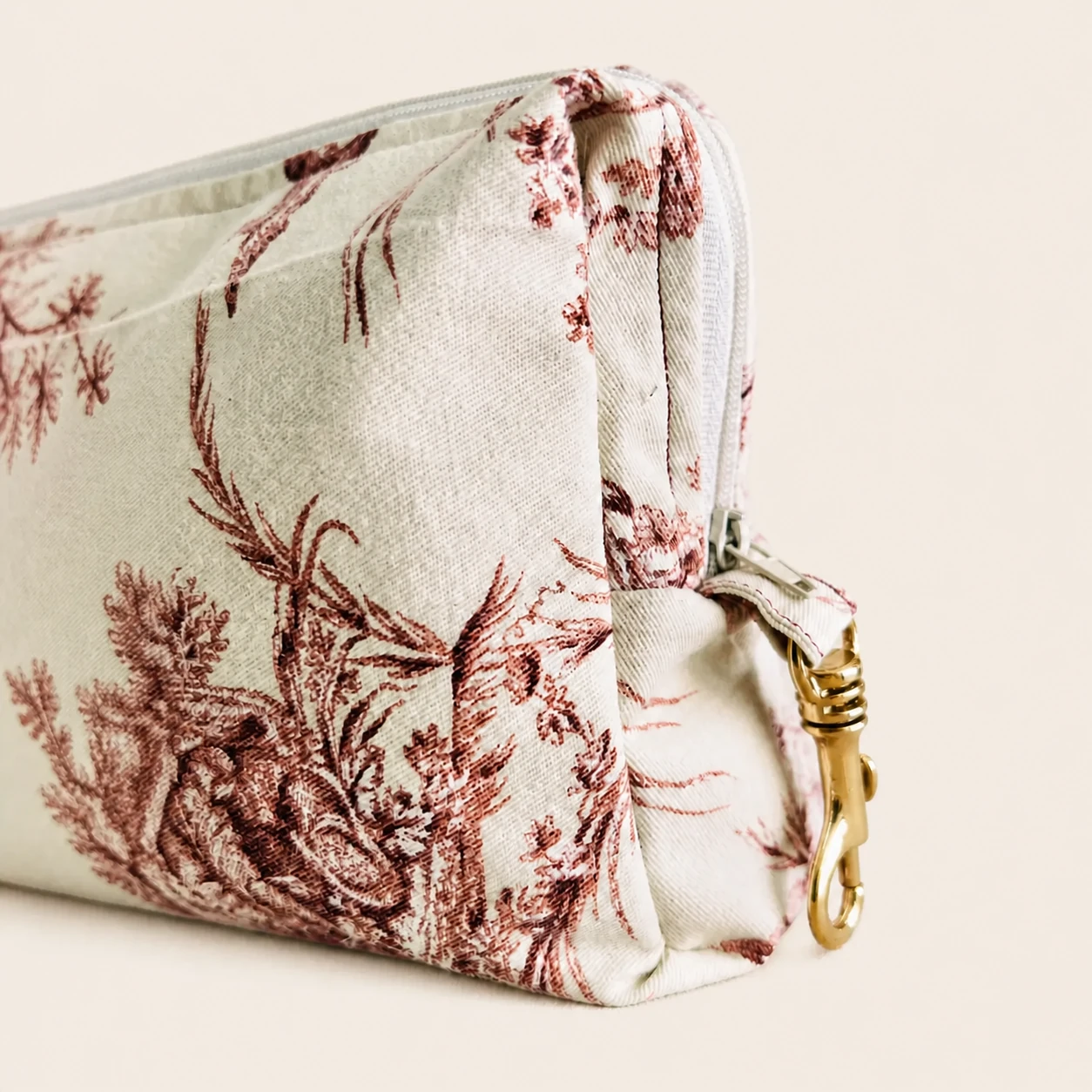 Side detail of the Red Toile Cotton Pouch with its zipper, textile tab and brass clasp.