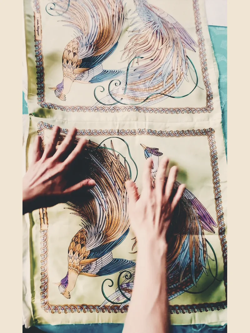 Two panels of a vintage Ferragamo silk cushion cover with stylized birds laid flat while hands arrange the delicate fabric