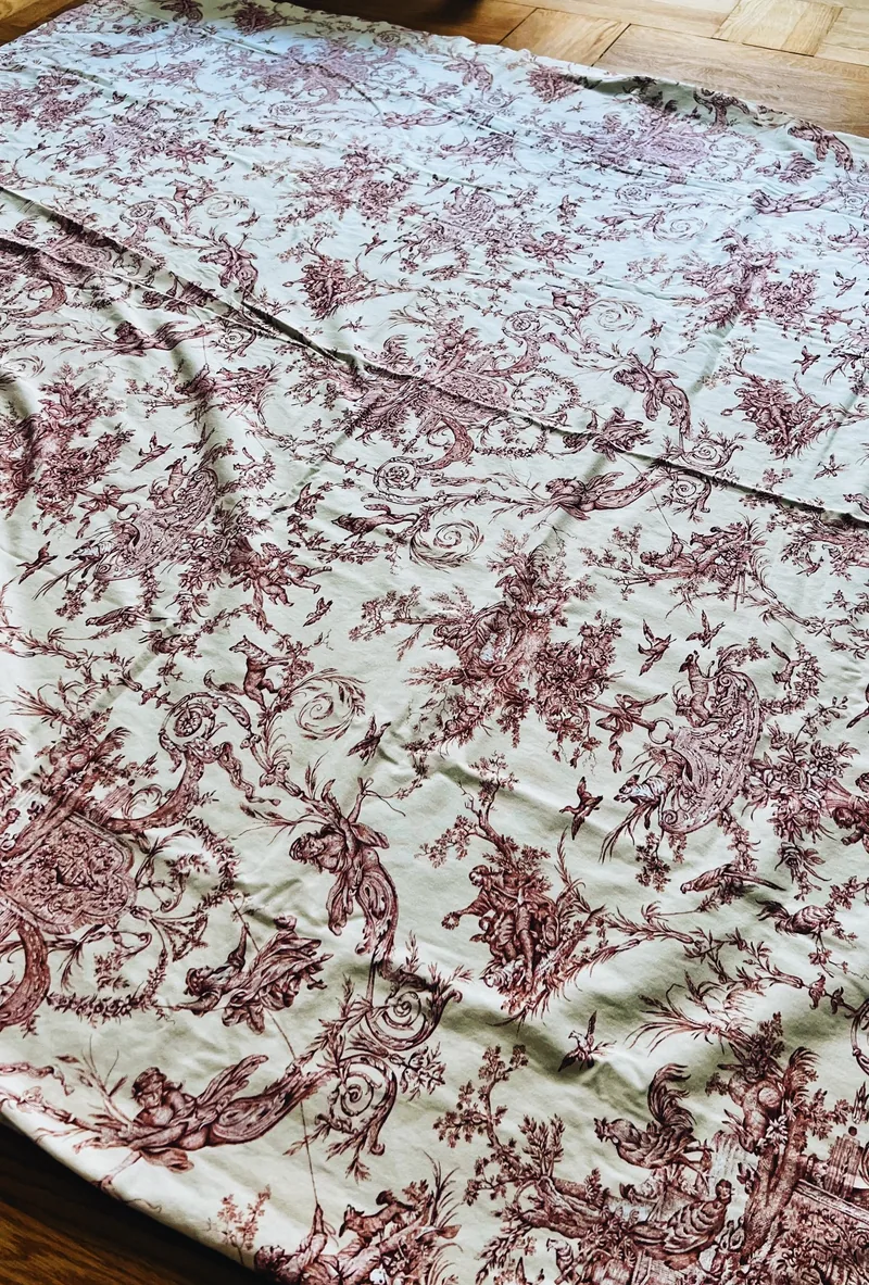 Cream toile tablecloth with burgundy pastoral print spread across a parquet floor